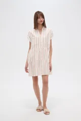 Vestido corto con cuello camisero, de corte holgado y mangas cortas. Presenta un diseño a rayas verticales en tonos beige y blanco, con volados en la falda y cierre frontal con botones.