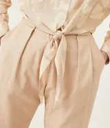Camisa de crepé color beige con estampado geométrico en tonos neutros, cuello camisero, manga larga y cierre con botones. Tiene un lazo frontal para atar.