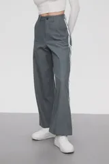 Pantalón gris de calce ancho y tiro alto, con bolsillos laterales y apliques de dos líneas blancas verticales en los laterales.