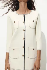 Chaqueta color crema de punto con cuello redondo y manga larga. Tiene bolsillos delanteros de plastrón, pespuntes combinados a contraste y cierre frontal con botones dorados.