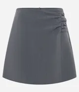Short pollera corto color gris, de sastrería con cierre por cremallera invisible en la parte de atrás, pences y detalle en fruncido en el lateral.