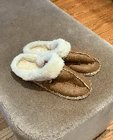 Pantuflas marrones de cuero lanar con interior de piel sintética blanca y suela de goma.