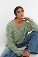 Sweater verde claro de tejido de punto calado con escote en V y mangas largas.