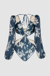Body de lycra azul con estampado floral blanco, escote en V, mangas largas abullonadas con hombreras y puños elásticos. Detalles de bordado en cordón y pedrería en escote y cintura.