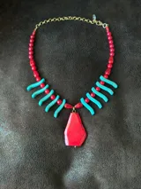 Collar de cuentas con dije central grande de piedra roja irregular, flanqueado por bastones turquesa y cuentas rojas redondas. La cadena es de eslabones finos con cierre regulable.