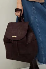 Mochila negra de símil gamuza con textura tipo reptil, diseño minimalista con solapa, cordón ajustable y bolsillos laterales.