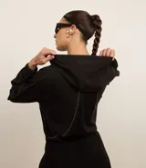 Campera deportiva cropped color negro, con capucha y mangas largas. Presenta cierre frontal, detalle reflectante y está confeccionada en tejido tecnológico.