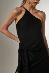 Vestido midi negro de bretel fino, con corte al cuerpo, cuello asimétrico y detalle de nudo en la cintura.