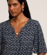 Blusa tipo bata de mangas cortas, confeccionada en viscosa con estampado de follaje en blanco sobre fondo azul marino. Tiene escote en V con detalle de abalorio en el centro.