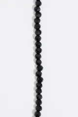 Pulsera de cuentas facetadas negras con cierre de mosquetón dorado y dije de corazón con logo grabado.