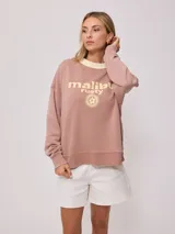 Sweater color ladrillo con cuello redondo en color crema. Estampado frontal con el texto 'Malibu Rusty' y un logo con forma de flor. Corte holgado.