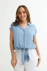 Camisa celeste de viscosa con cuello camisero, mangas cortas y cierre frontal con botones. Tiene un lazo en el ruedo para anudar.