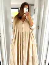 Vestido camisero largo color beige con rayas verticales blancas, cuello camisero, abotonadura frontal y mangas 3/4 con puños blancos.