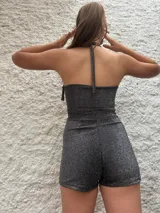 Mono corto de lurex color gris, con escote halter asimétrico y calce ajustado.