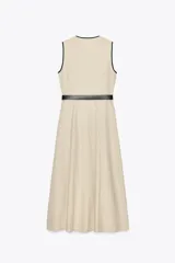 Vestido midi de lino color beige, con escote cruzado en pico y sin mangas. Presenta vivos a contraste en negro y cinturón con hebilla forrada. Cierre frontal con botones.