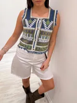 Chaleco corto de denim azul con bordado artesanal en tonos naranja, blanco y marrón. Tiene escote cuadrado, cierre de botones y terminaciones desflecadas.