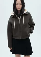 Chaqueta negra corta con capucha gris desmontable y ajustable con cordones. Presenta cuello camisero, cierre de cremallera doble, bolsillos laterales y bajo con goma elástica.