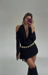 Vestido corto negro con escote pronunciado en V y drapeado en el busto. Presenta mangas largas con aberturas en los hombros (cold shoulder) y puños acampanados.
