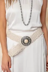 Cinto color crudo trenzado con hebilla metálica plateada con piedra central color crema.