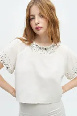 Blusa color crudo de lino y algodón, de manga corta con escote redondo y bordado de lentejuelas y mostacillas en el cuello y mangas.