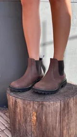 Botas Chelsea de cuero color marrón, con elástico lateral, suela negra gruesa y pespuntes blancos.