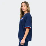 Remera blanca de mujer con cuello y mangas con detalles tricolor (azul, blanco y rojo), logo de Umbro bordado en negro y escudo del Club Nacional de Football estampado.