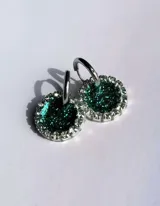 Aros colgantes con forma circular, hechos de resina color lila y borde de strass plateado. El aro es de acero quirúrgico plateado.