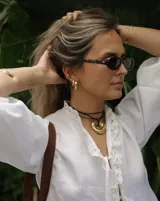 Collar con dije dorado irregular con agujero central, colgando de cordón negro ajustable.