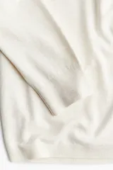 Sweater corto de punto fino color crema, con escote en V, hombros caídos y terminaciones acanaladas en puños y bajo.