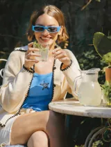 Cardigan tejido color crema con cuello polo, cierre con botones y ribete negro en cuello, puños y ruedo.