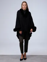 Ruana o poncho negro de tejido suave, con cuello y puños adornados con apliques de piel sintética (faux fur).