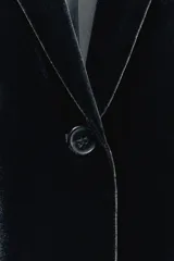Blazer de terciopelo negro con cuello solapa de muescas, manga larga con abertura y botones, bolsillos con solapa y forro interior.