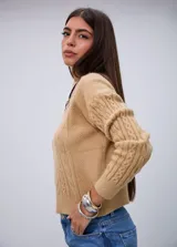 Sweater de punto color beige con cuello redondo, mangas largas y detalles de trenzas en el frente y las mangas.