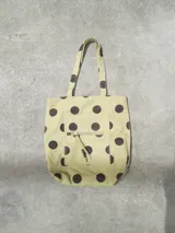 Bolso tote de tela color beige con estampado de lunares marrones. Tiene dos asas de hombro y un bolsillo frontal con cierre.