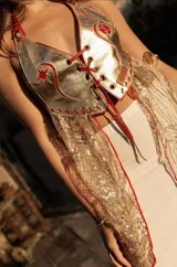 Top de cuero dorado brillante con tela bordada con canutillos dorados que cae a los costados y detalles en cuero rojo. Se ajusta en cuello y espalda.