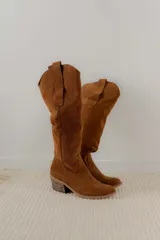 Bota alta de cuero color beige, estilo texana, con caña alta y taco bajo.