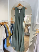 Vestido largo sin mangas, color marrón oscuro, con escote en V y corte amplio que cae hasta el tobillo. El ruedo tiene un acabado deshilachado.