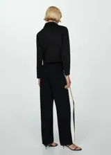 Chaqueta corta negra con cuello camisero, cierre frontal con botones, dos bolsillos laterales y forro interior.