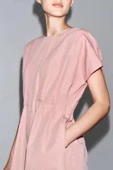 Vestido midi color marrón confeccionado en hilatura con mezcla de algodón y lino. Tiene cuello redondo, manga corta caída y detalle de pliegues en la cintura. Cierre en la espalda con abertura y botón.