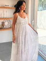 Vestido largo blanco de algodón con tirantes finos, escote en V con detalle de encaje calado y bordado. Falda con múltiples volados y terminaciones con flecos/borlas.