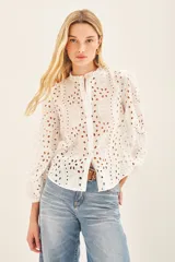 Camisa celeste de broderie de algodón con calado de hojas. Tiene cuello redondo con volados, mangas largas abullonadas con puños elásticos y cierre frontal con botones.