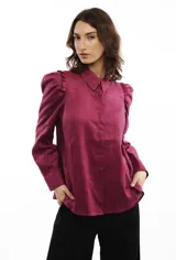 Camisa color fucsia de lino, con cuello clásico, mangas largas abullonadas con volados en los hombros, corte recto y cierre frontal con botones.