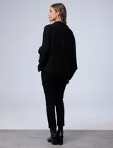 Cardigan negro de tejido suave, estilo poncho o capa, con cuello tipo chal y mangas amplias.