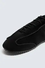 Zapatilla de cordones color negro, con capellada de cuero serraje, horma redonda y suela ultrafina.