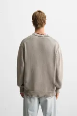 Jersey de punto color beige, de corte holgado, con cuello redondo y manga larga. Tiene efecto lavado y rotos en toda la prenda.