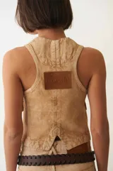 Chaleco denim color arena con efecto acid wash, cuello en V, cierre frontal con botones y dos bolsillos con solapa en el pecho.