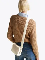 Bandolera Tommy Hilfiger color crema con correa ancha de tela con el logo de la marca en color blanco. Tiene el logo de la marca en dorado en la parte frontal y herrajes dorados.