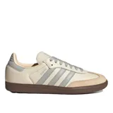 Championes Adidas Samba OG W, color beige claro con detalles en gris claro y suela de goma marrón. Presentan las tres franjas características de Adidas en gris y la palabra "SAMBA" estampada en el lateral.