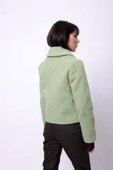 Campera corta de poliéster texturizado color verde oscuro, con cuello camisero, cierre frontal con botones a presión, bolsillos delanteros y forro interior. Incluye pins decorativos.