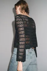 Jersey corto de punto calado negro, con cuello redondo amplio y mangas largas acampanadas.